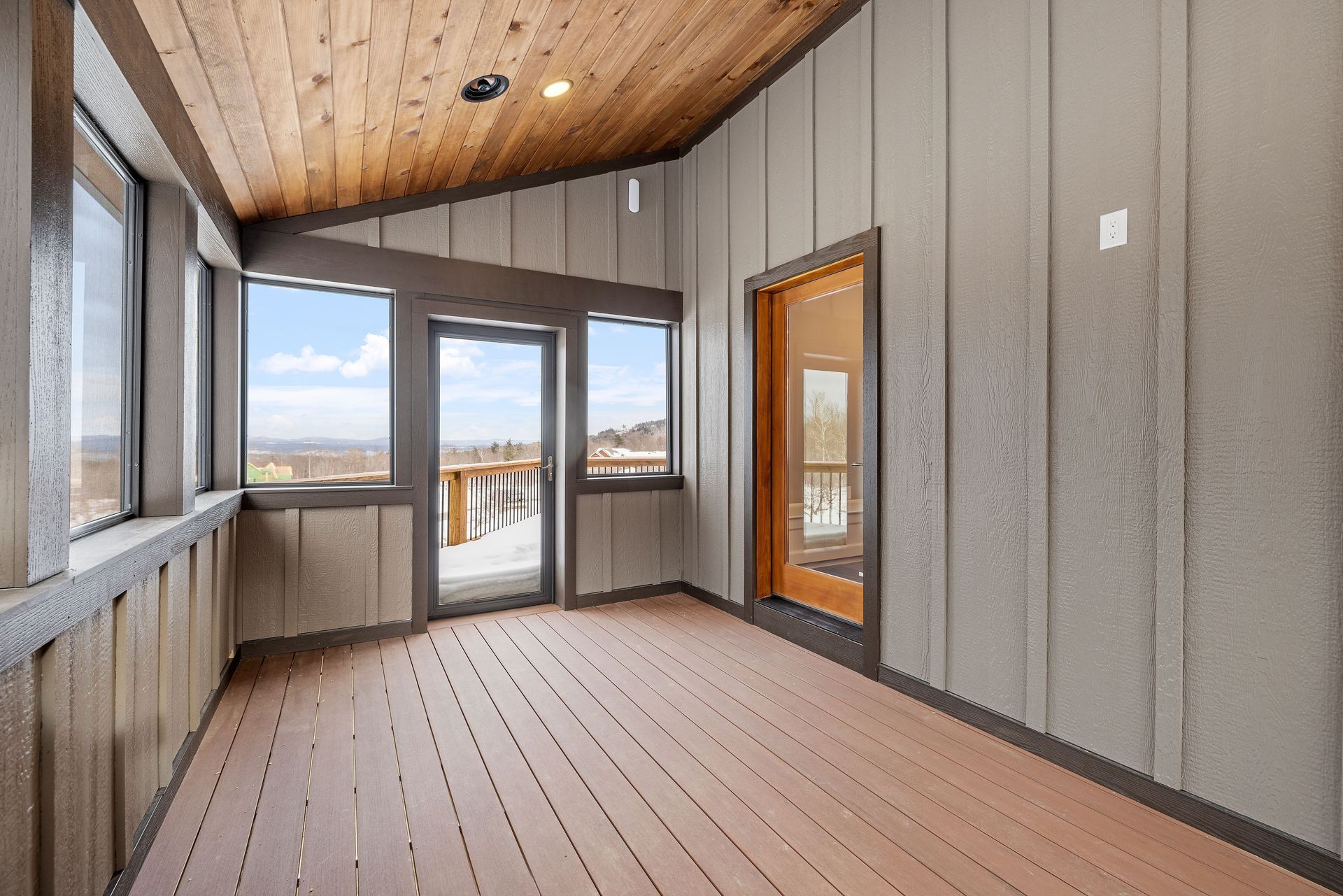 Sunroom with wood ceiling and floor, gray walls, and large windows with a view.