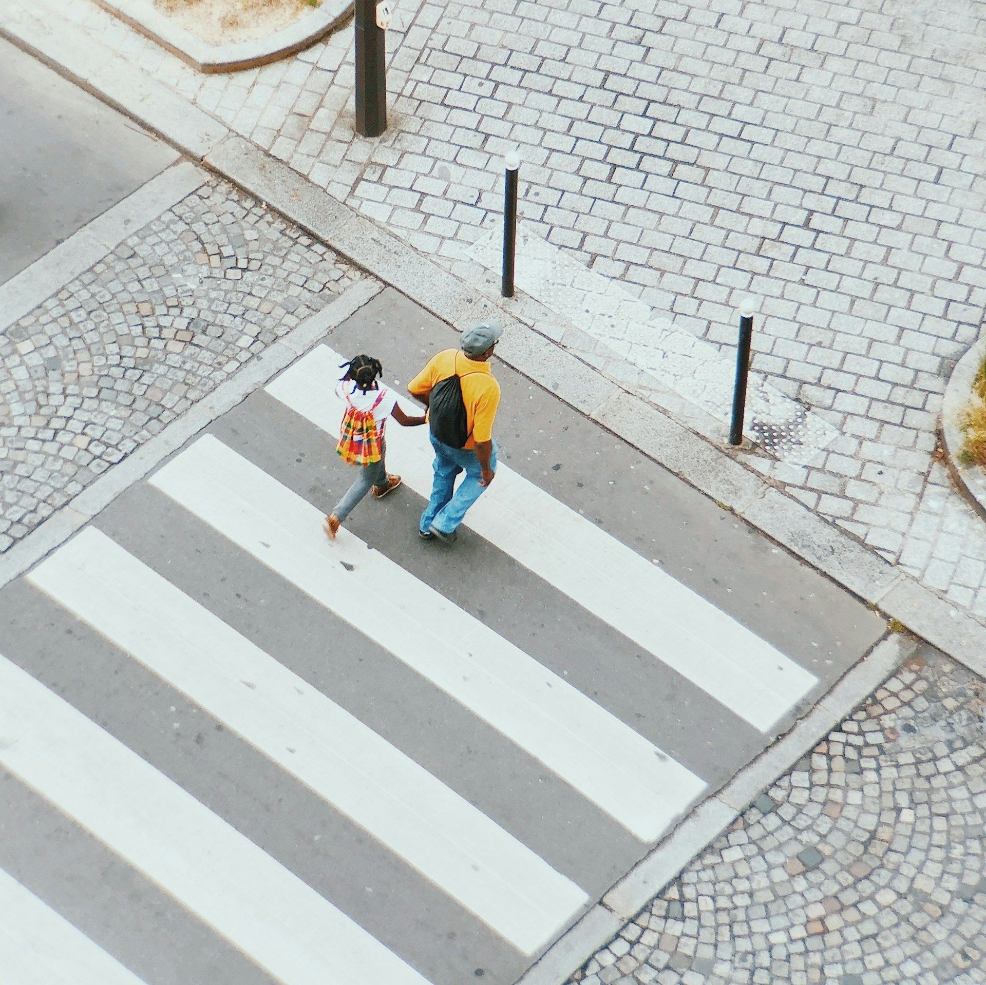 Two people with umbrellas crossing a zebra crossing on a cobblestone street.