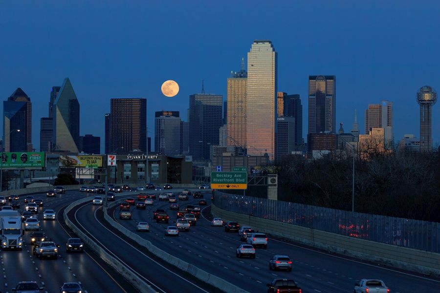 City skyline at dusk with a full moon above a busy highway and moving traffic