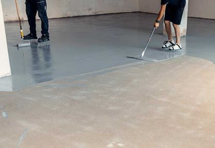 Construction workers applying grey epoxy resin in an industrial hall