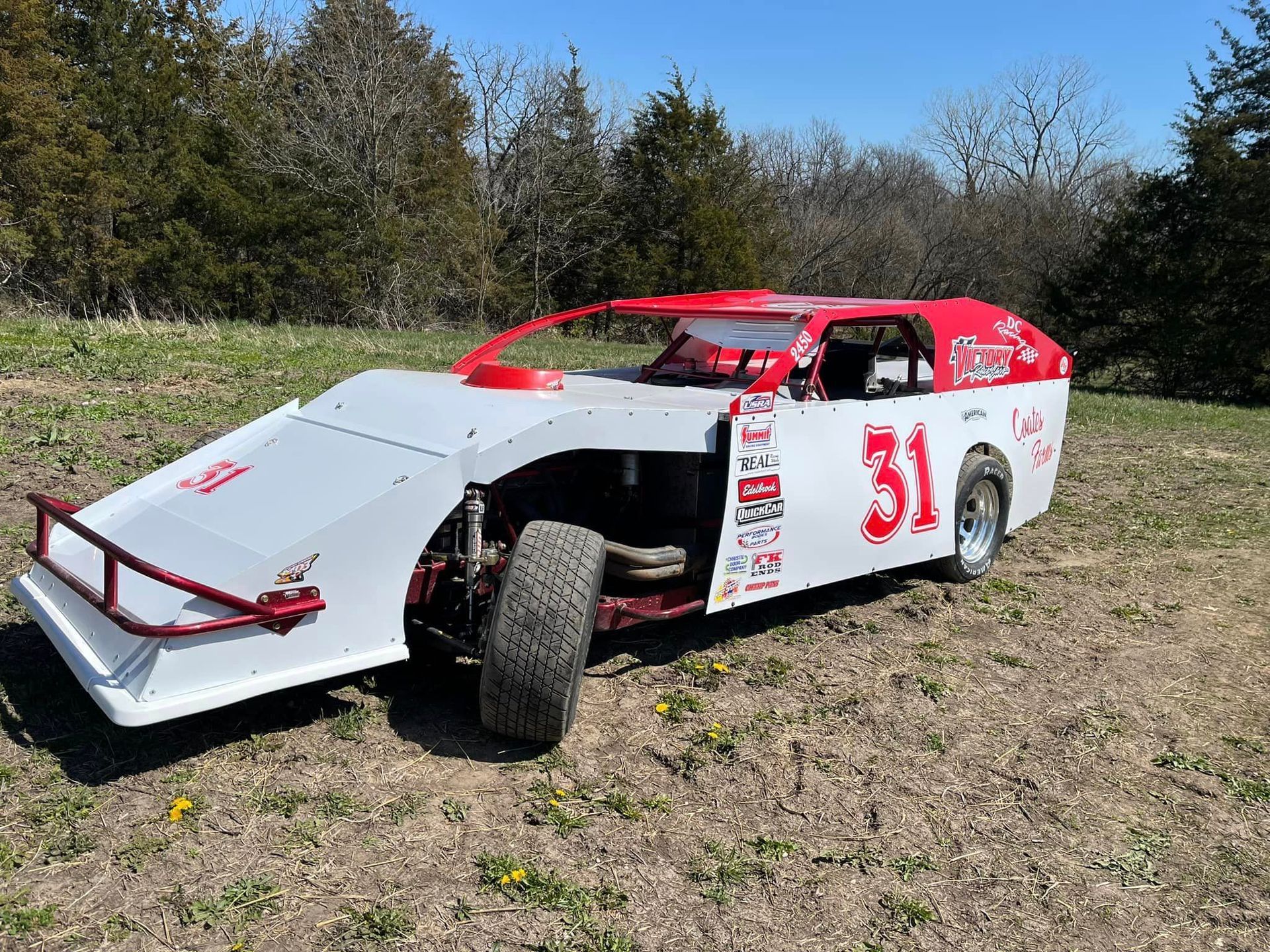 A white and red race car with the number 31 on the side is parked in a field.