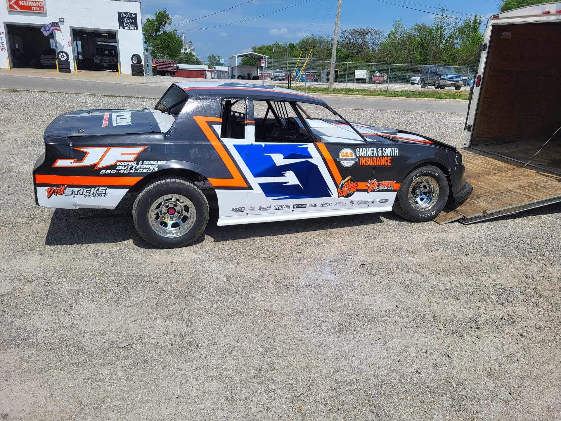 A race car is parked in a gravel lot next to a trailer.