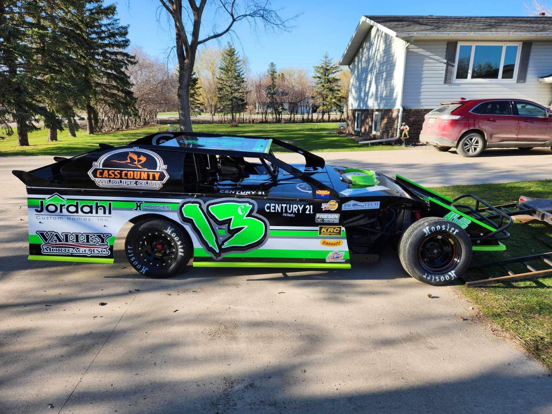 A green and white race car is parked in front of a house.