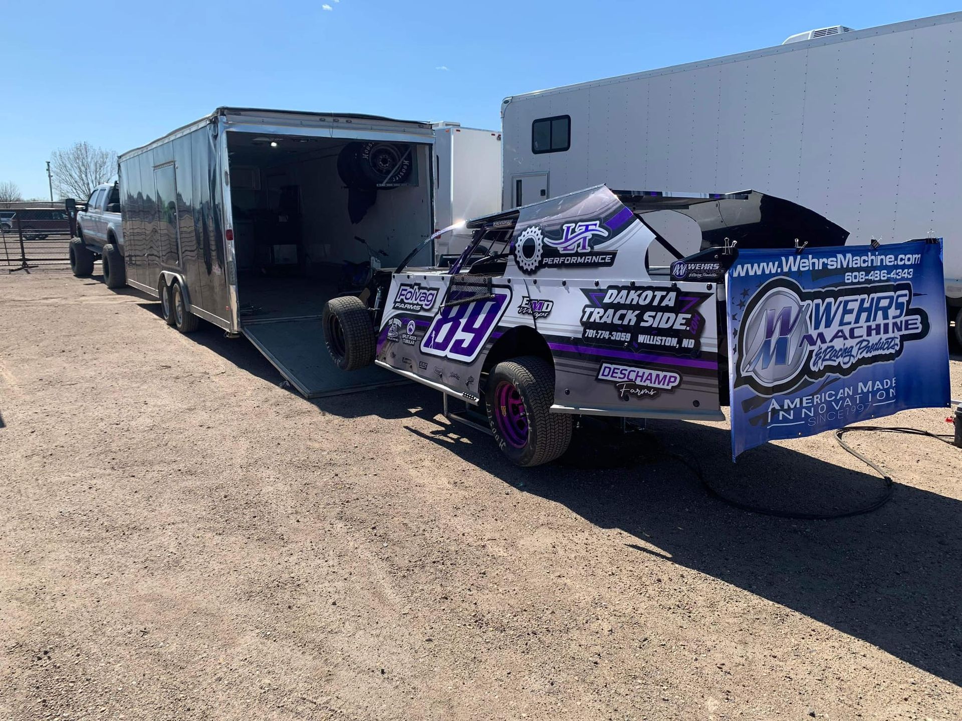 A race car is being towed by a trailer in a dirt field.