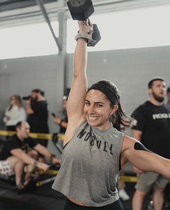 A woman is lifting a dumbbell over her head in a gym.