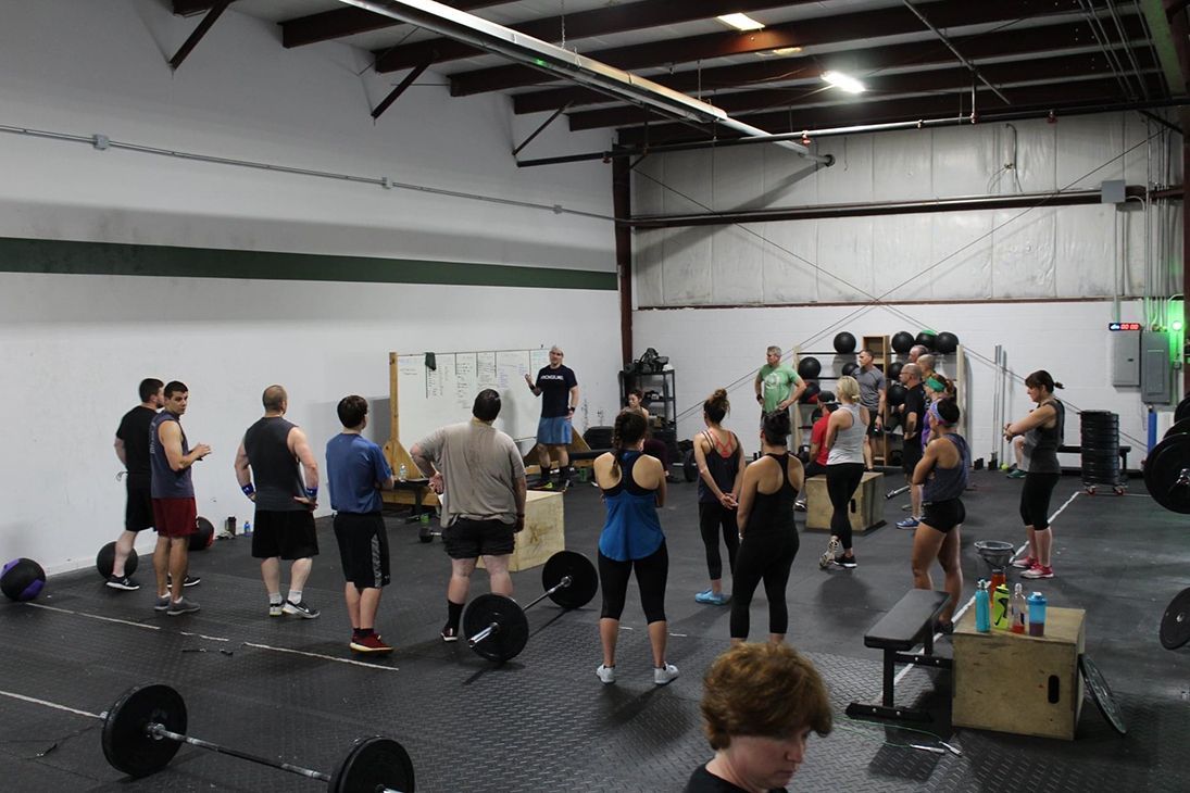 A group of people are standing in a gym holding barbells.