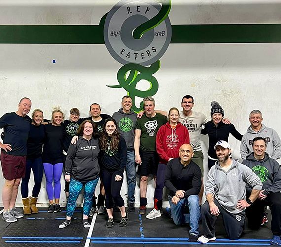 A group of people posing for a picture in front of a barbell that says faters