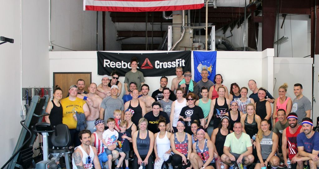 A large group of people are posing for a picture in front of a reebok crossfit sign.