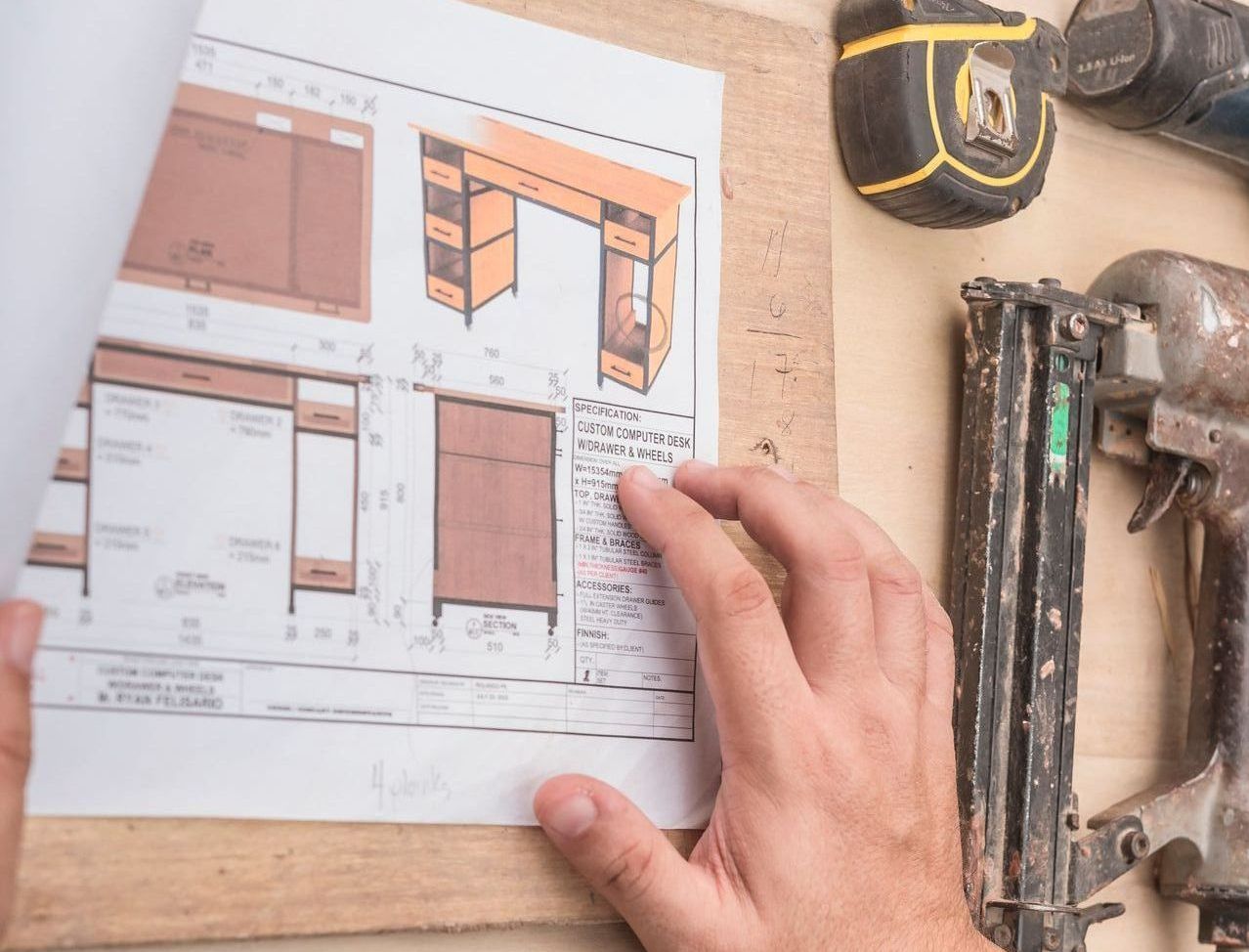 A person is holding a piece of paper with a drawing of a desk on it looking at measurements for custom furniture