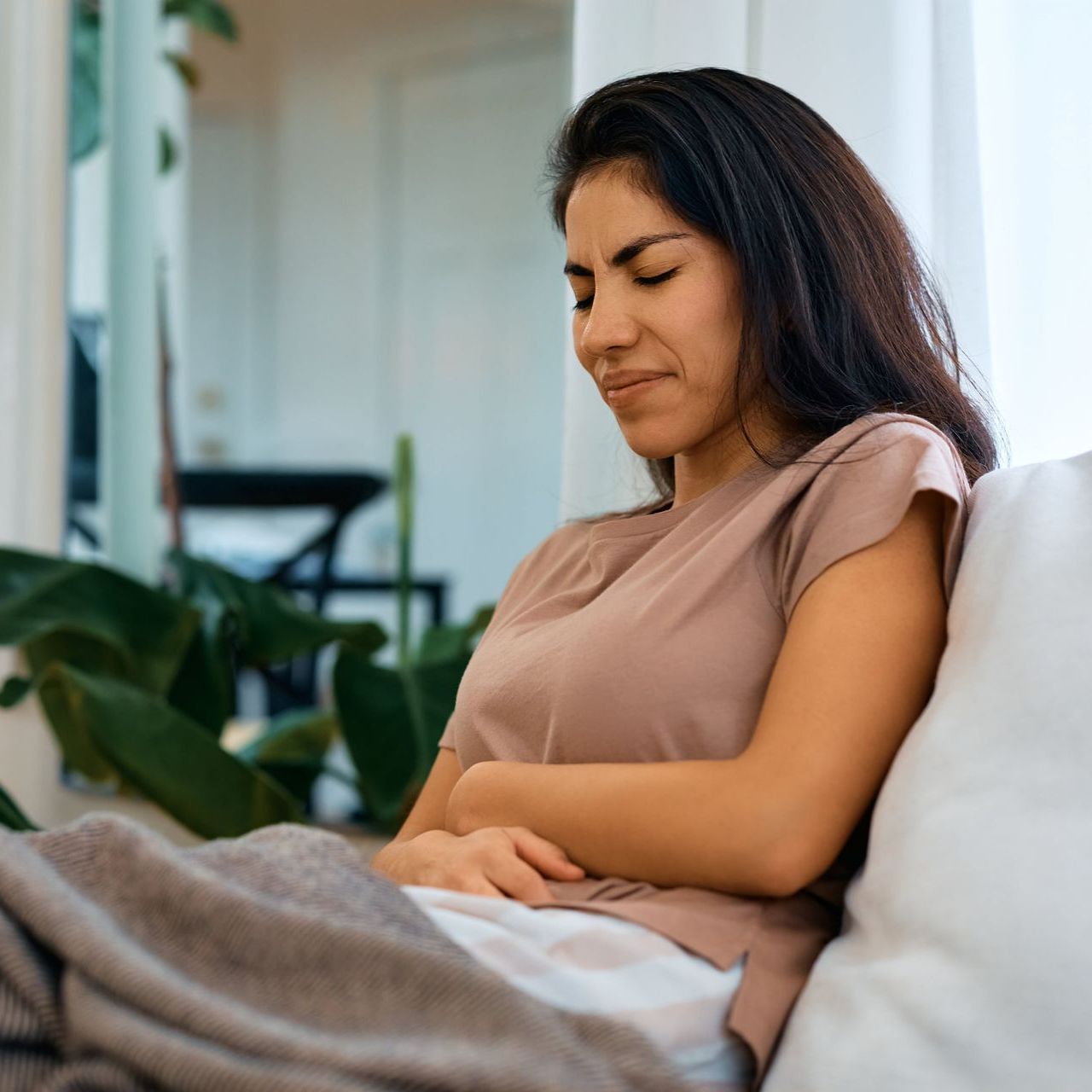 A woman sitting on a couch holding her stomach in pain