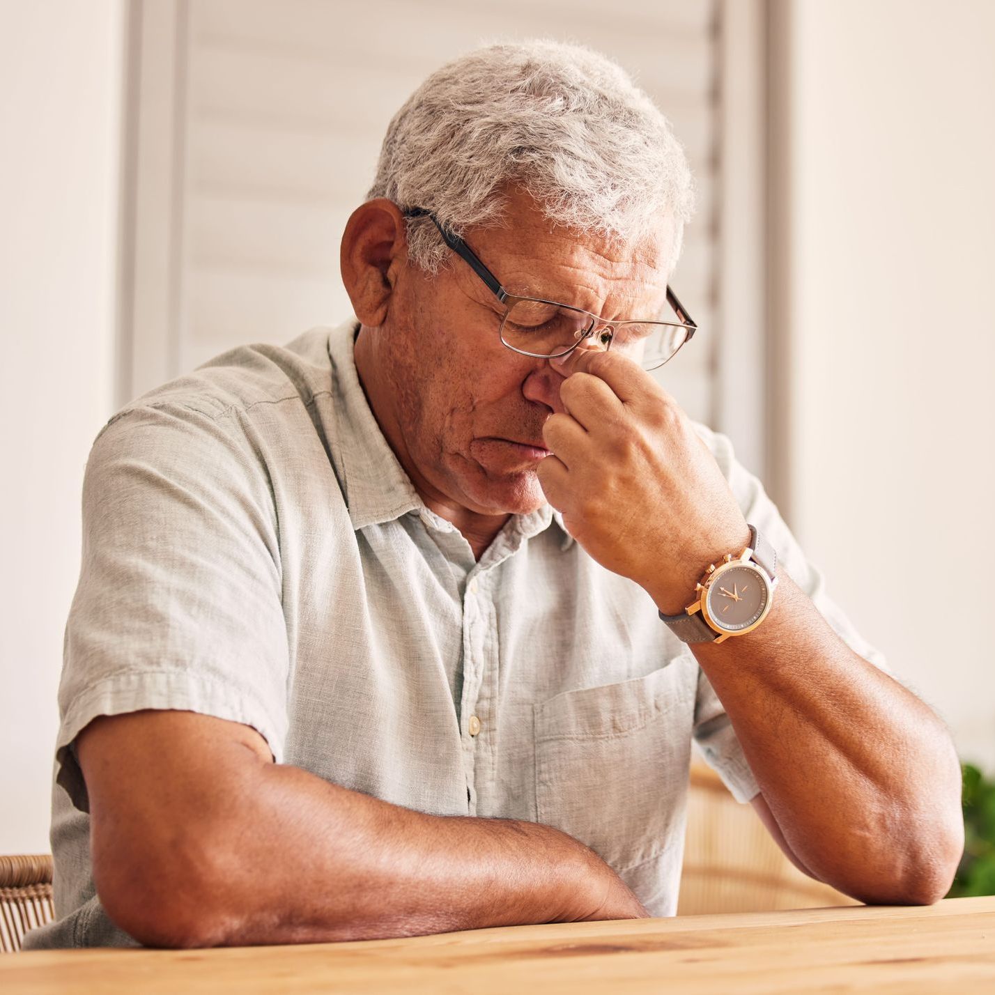 An older man pinching his nose and looking down in distress