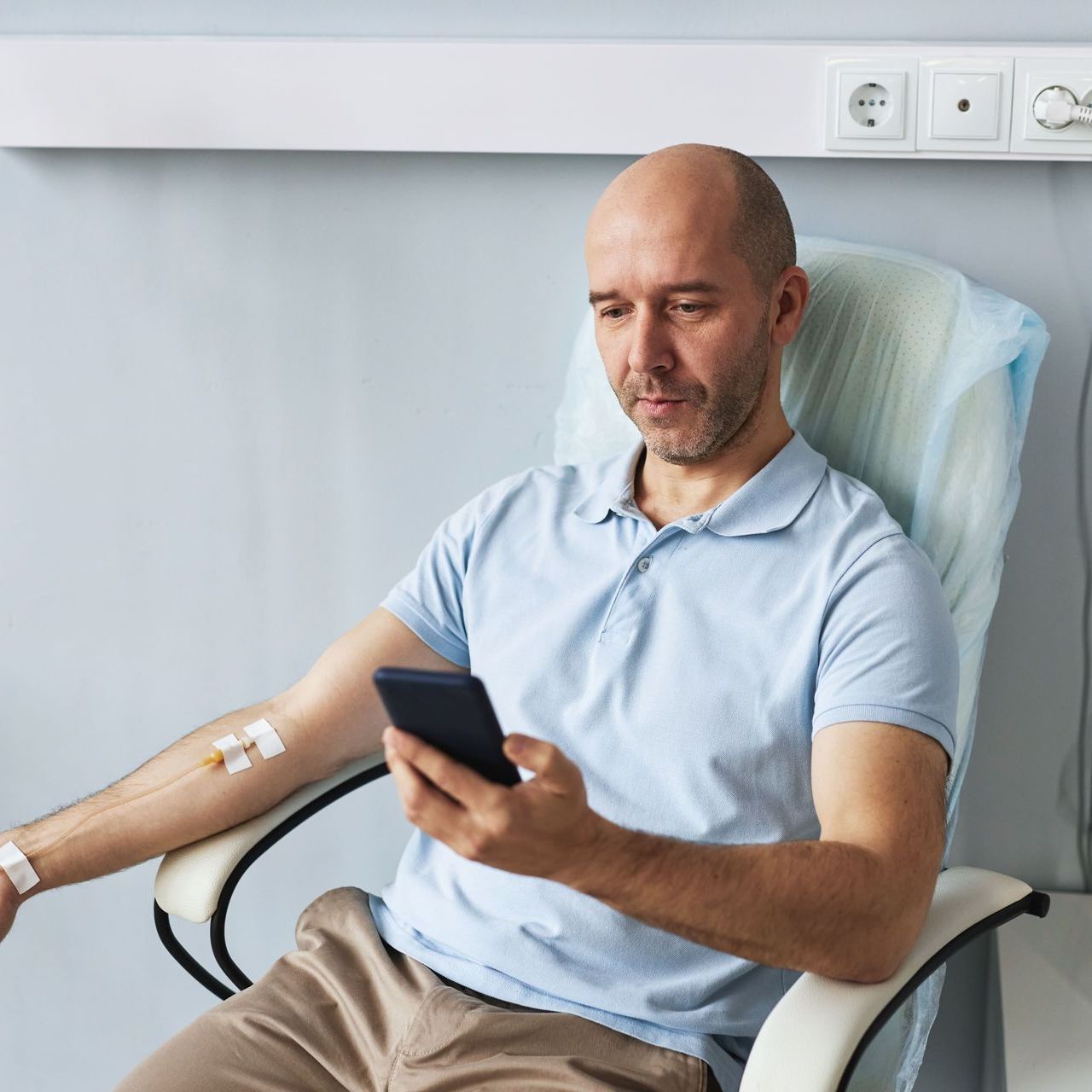 A man is sitting in a hospital chair looking at his phone