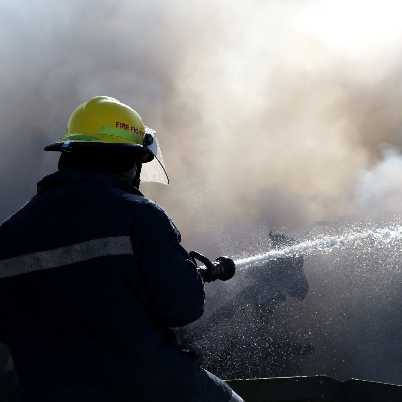 A fireman wearing a yellow helmet spraying water from a hose