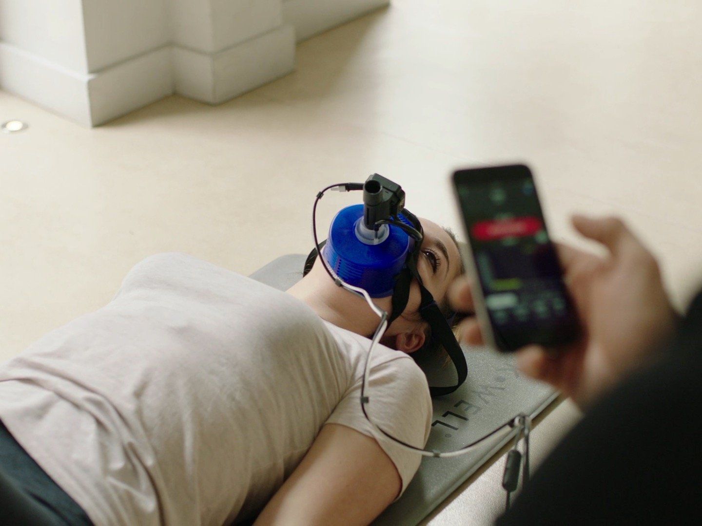 A woman is laying on a yoga mat while a man holds a cell phone.