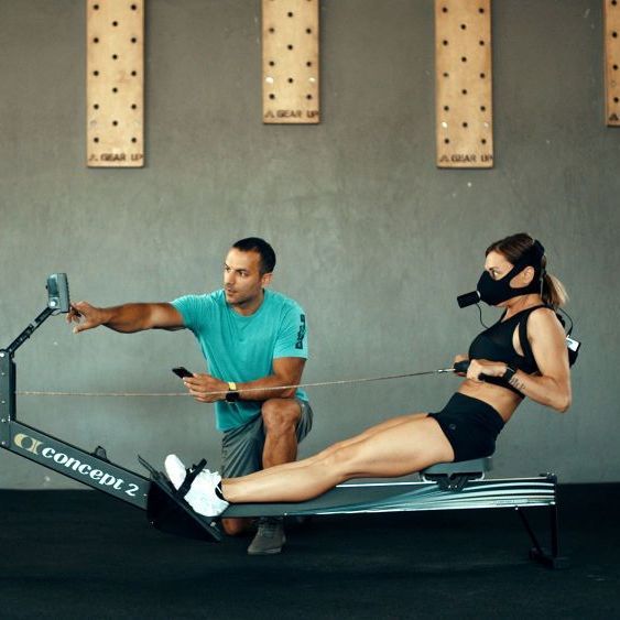 A man is teaching a woman how to use a concept 2 rowing machine