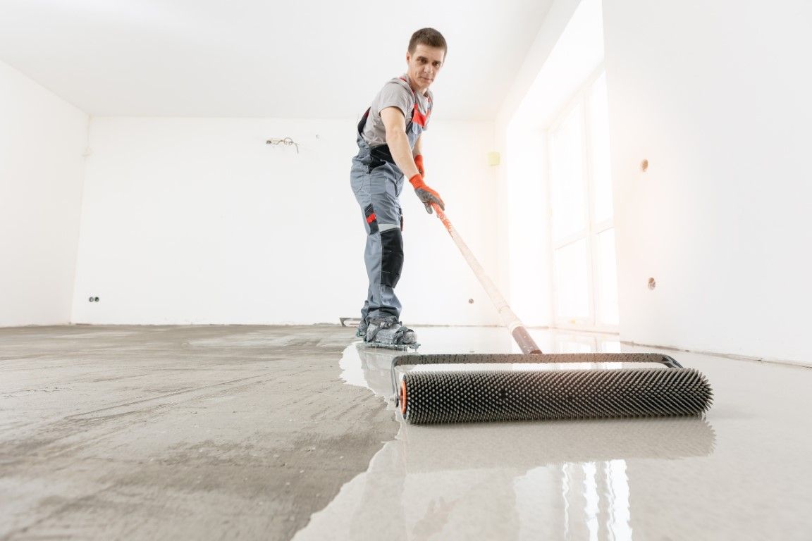 A man is painting a concrete floor with a roller.