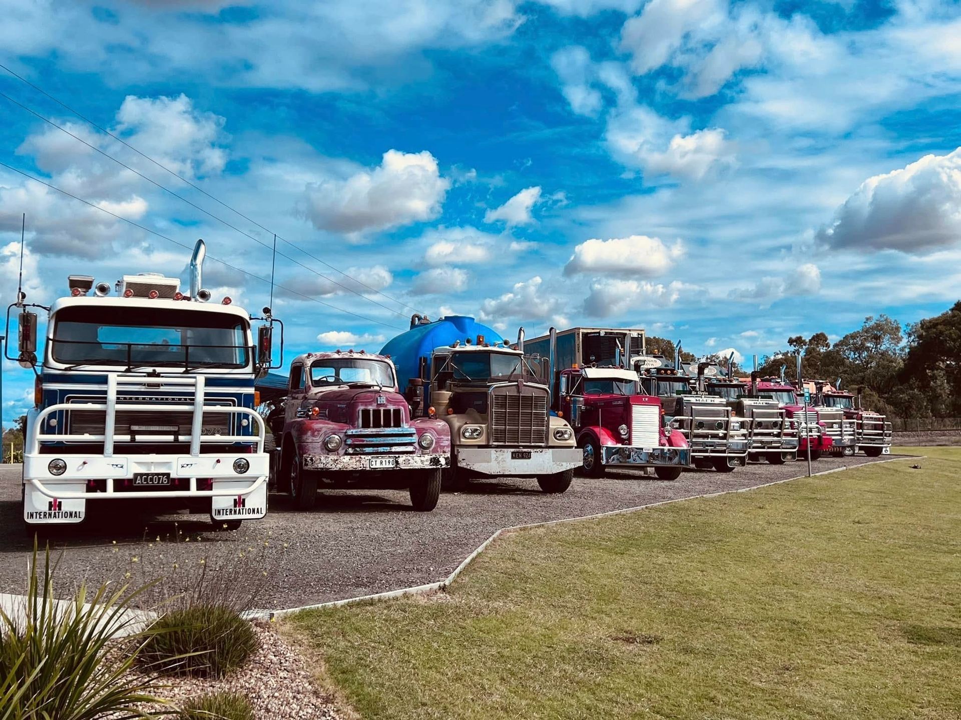 A Row of Colorful Semi-trucks Parked on Gravel, Under a Blue Cloudy Sky