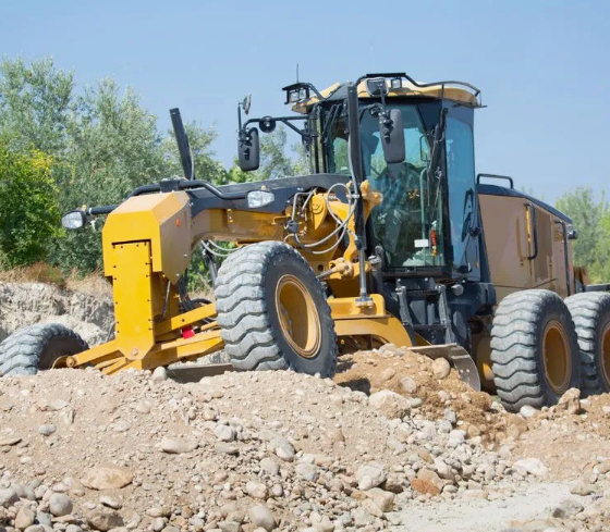 A yellow grader is sitting on top of a pile of dirt.