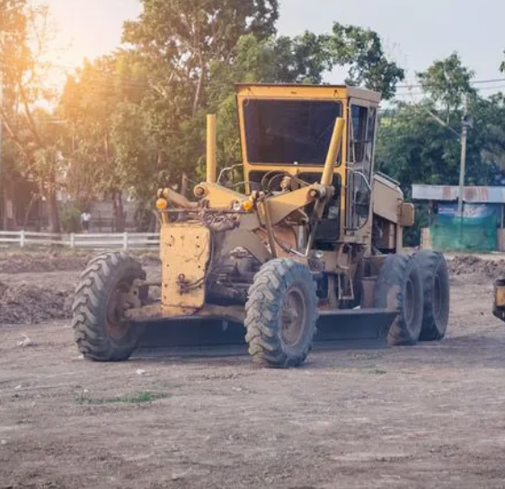 A yellow grader is parked in a dirt field.