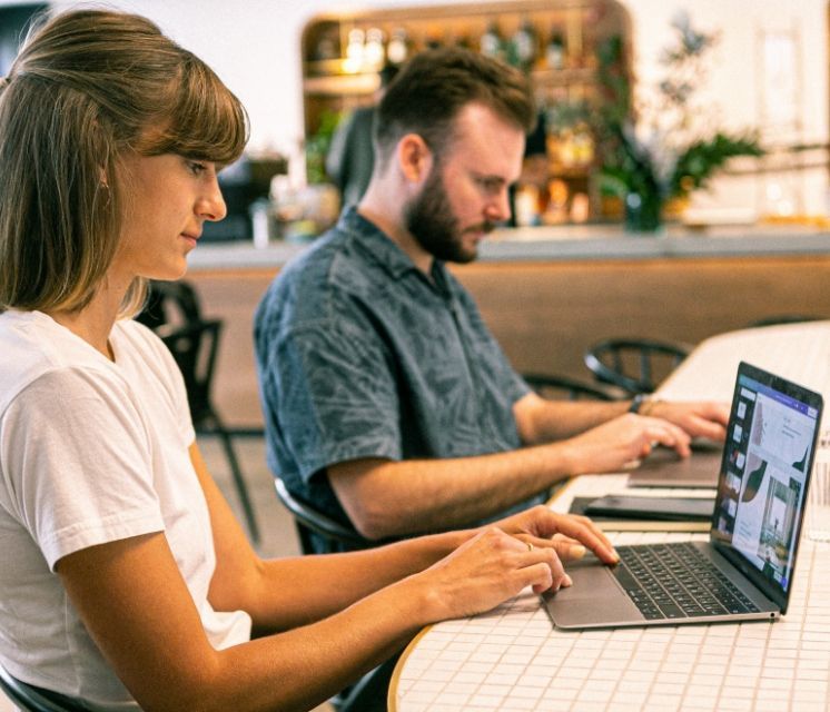 A man and a woman are sitting at a table using laptops.