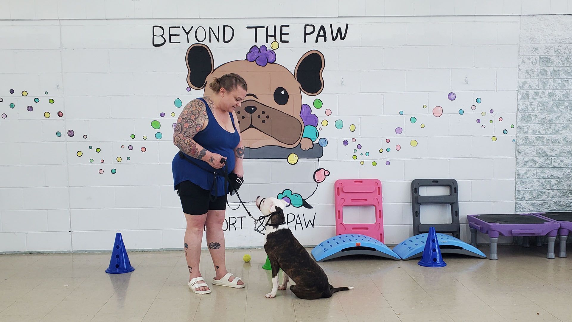 A woman is standing next to a dog in front of a mural that says beyond the paw.