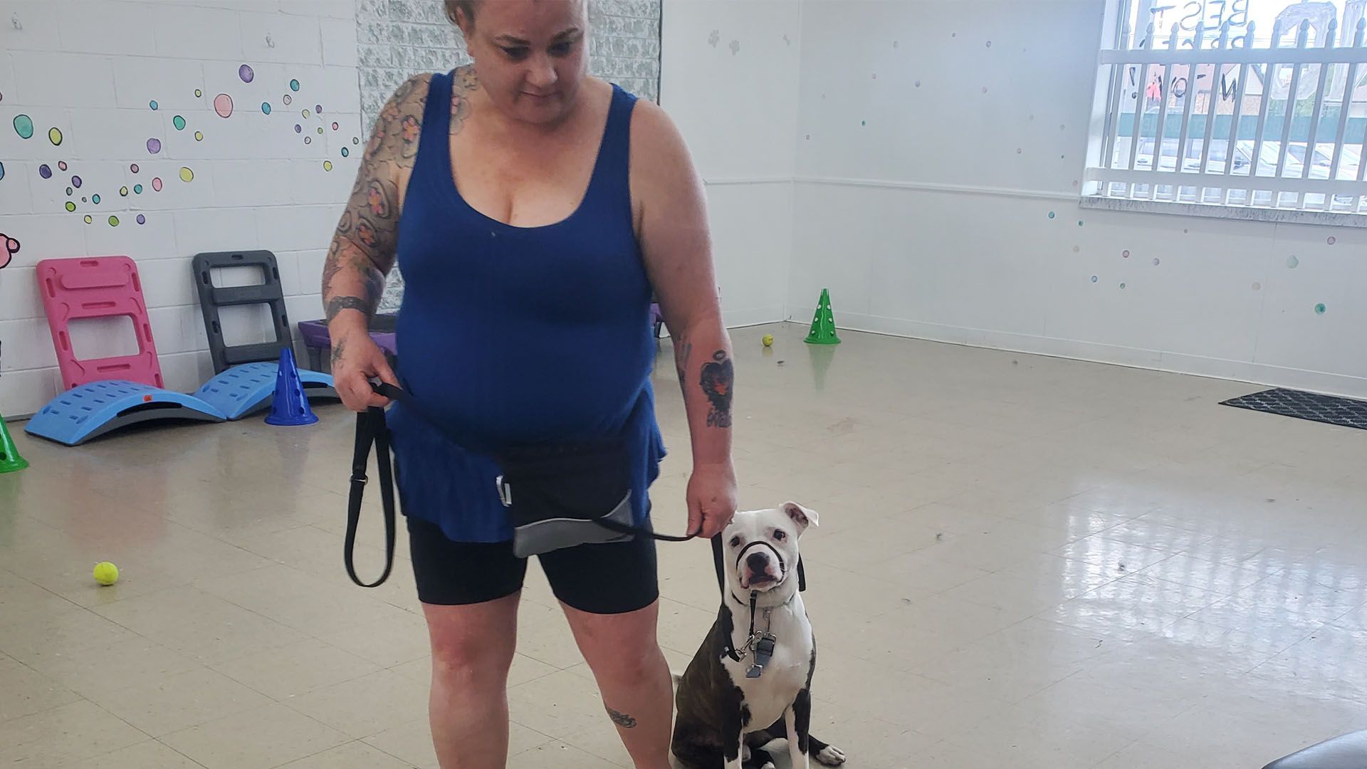 A woman is standing next to a dog on a leash in a room.