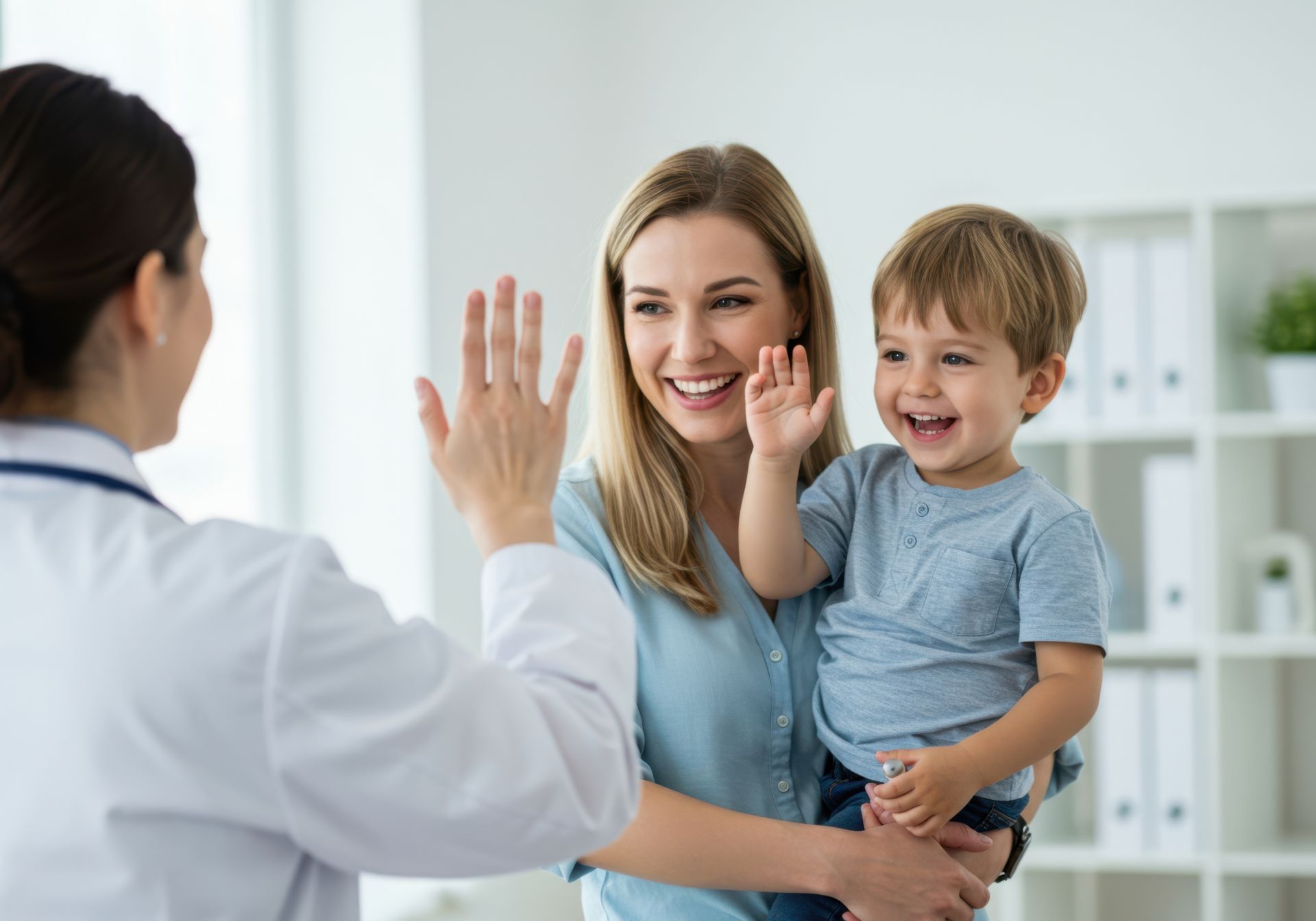 Doctor high-fives a happy child held by a smiling parent in a doctor's office.