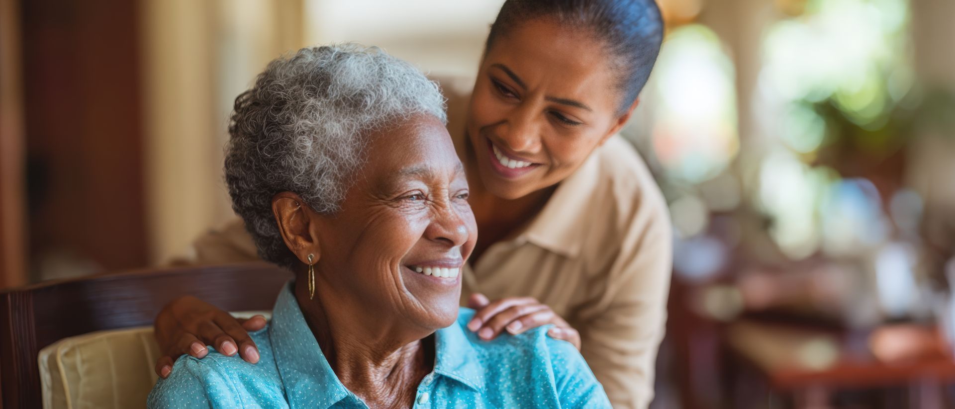 Woman with gray hair smiles while another woman places hands on her shoulders.