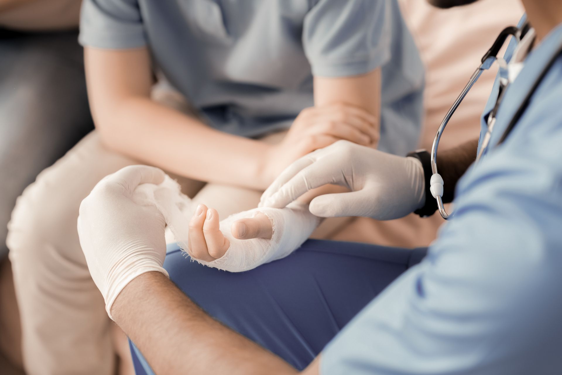 Doctor wrapping a patient's bandaged wrist with white gauze; close-up view.
