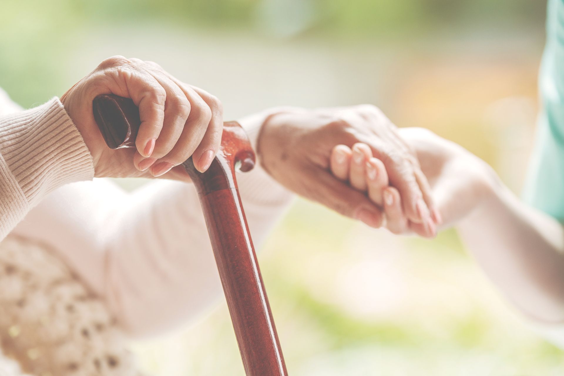 An older person's hands holding a cane, another hand gently helping.