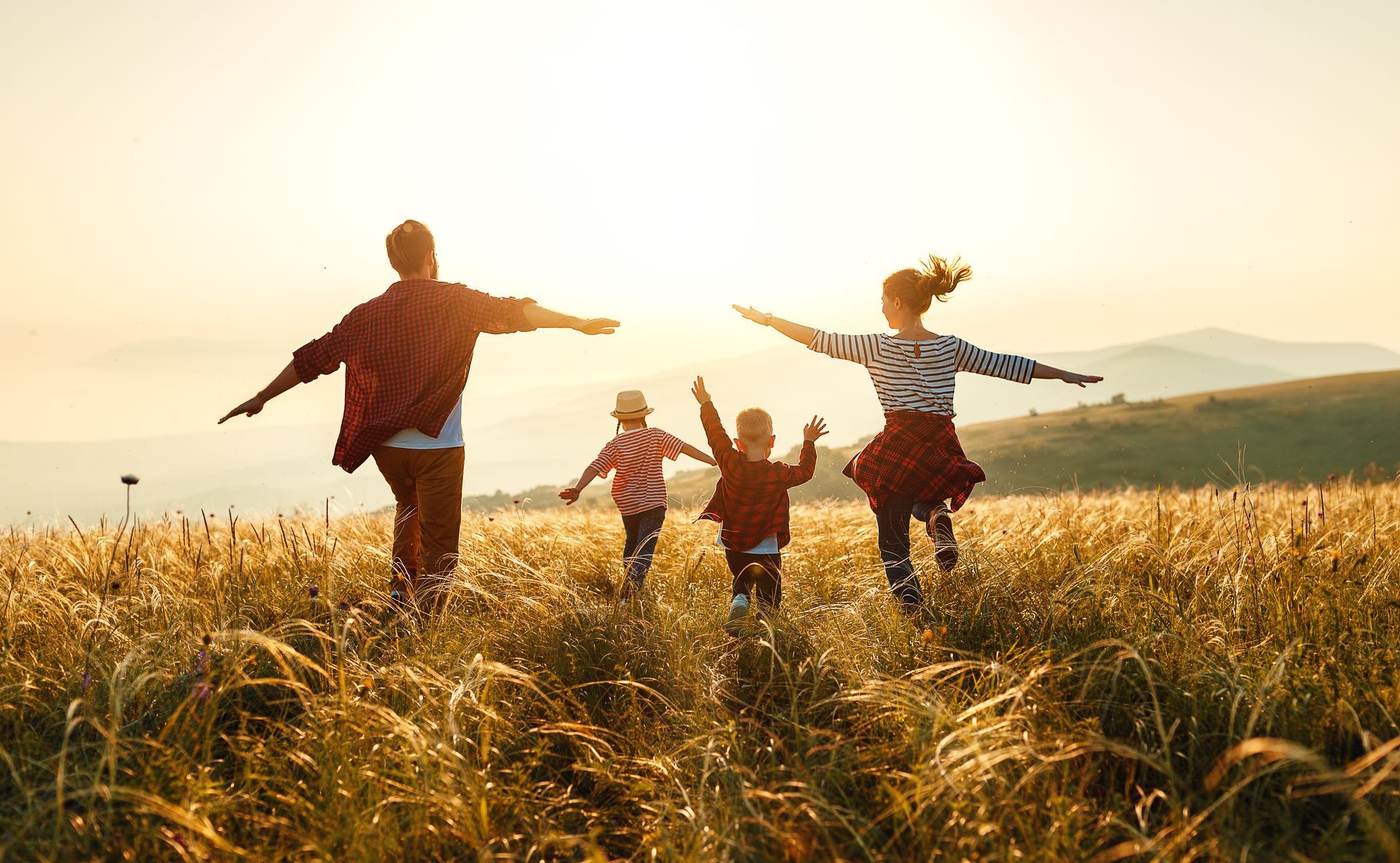 Family running joyfully through a golden field at sunset with arms outstretched.