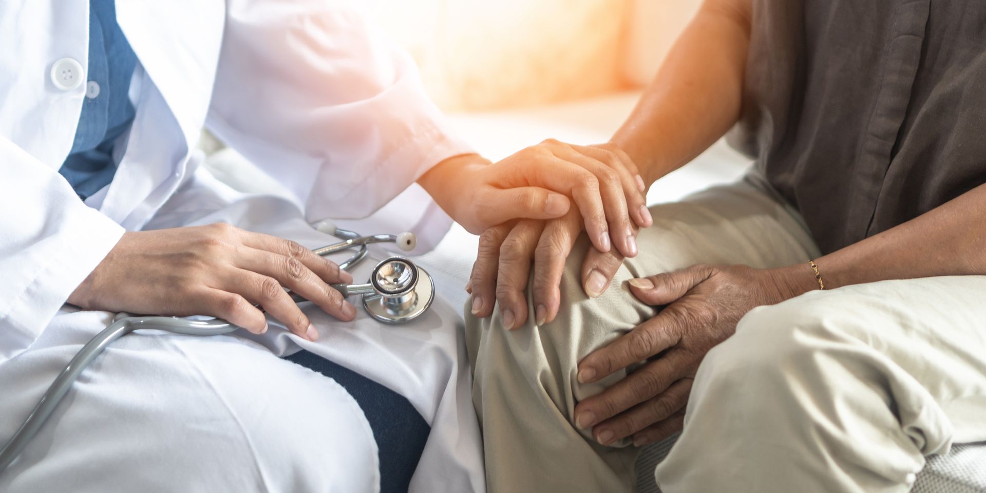 Doctor holding patient's hands for support; stethoscope on lap.