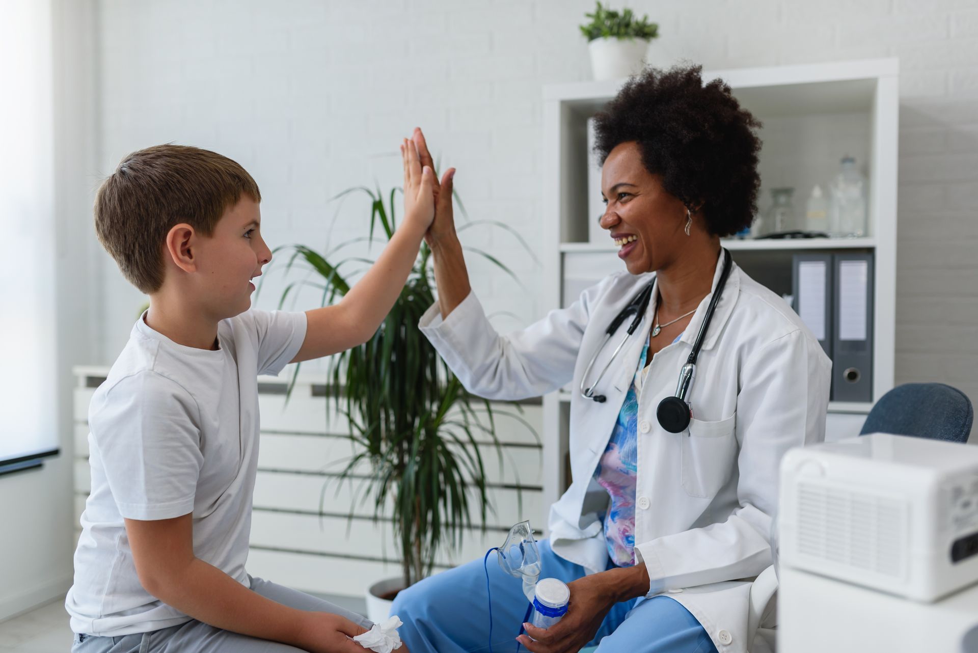 Doctor and child high-fiving in a medical office; smiling, positive interaction.