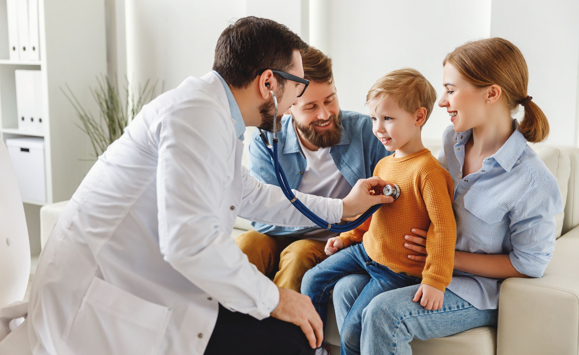 Doctor using a stethoscope on a child; parents present. Interior, neutral tones.