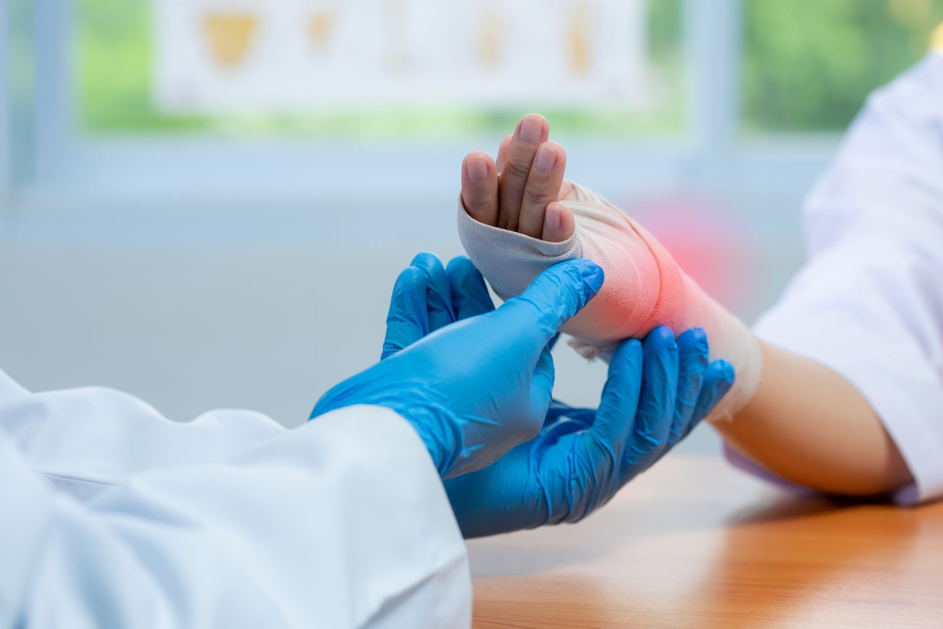 Doctor in blue gloves examines a patient's injured wrist wrapped in a bandage, with a red area indicating pain.