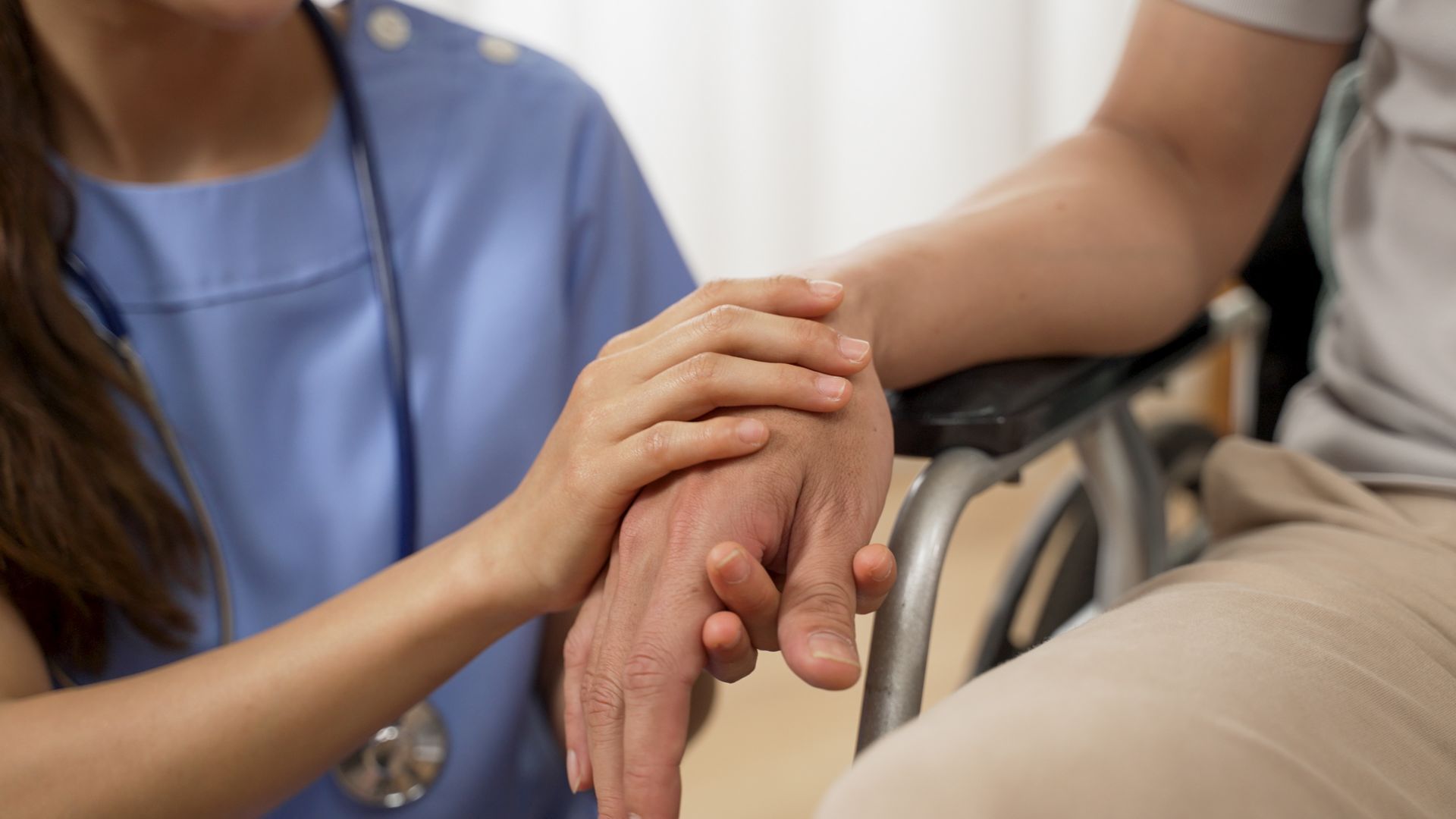 Nurse holding a patient's hand for comfort, seated in a wheelchair.