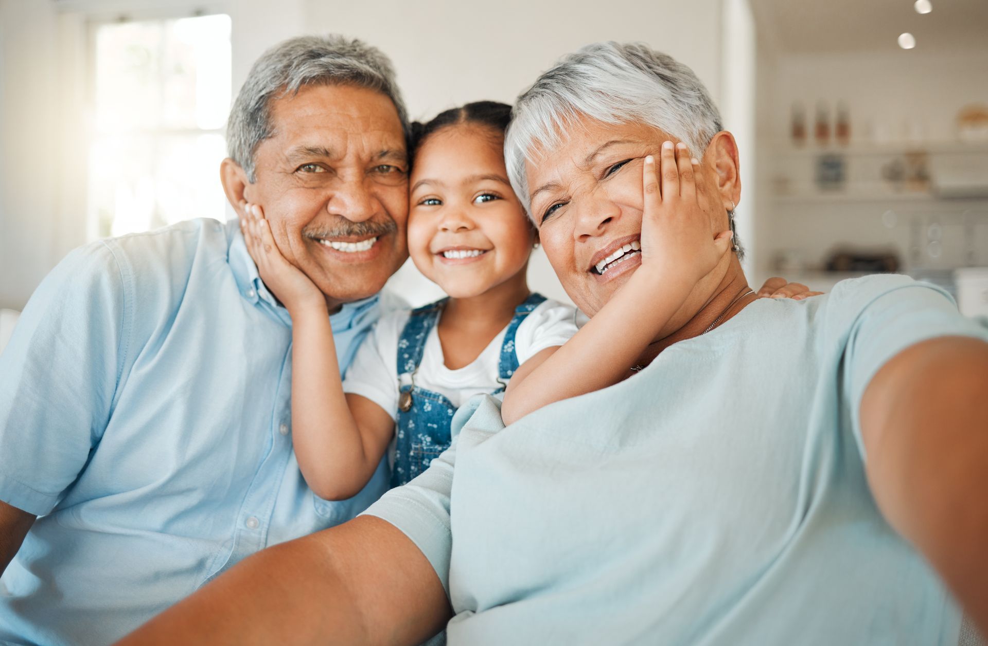 Grandparents and granddaughter smiling, indoors, close-up. They are embracing and taking a selfie.