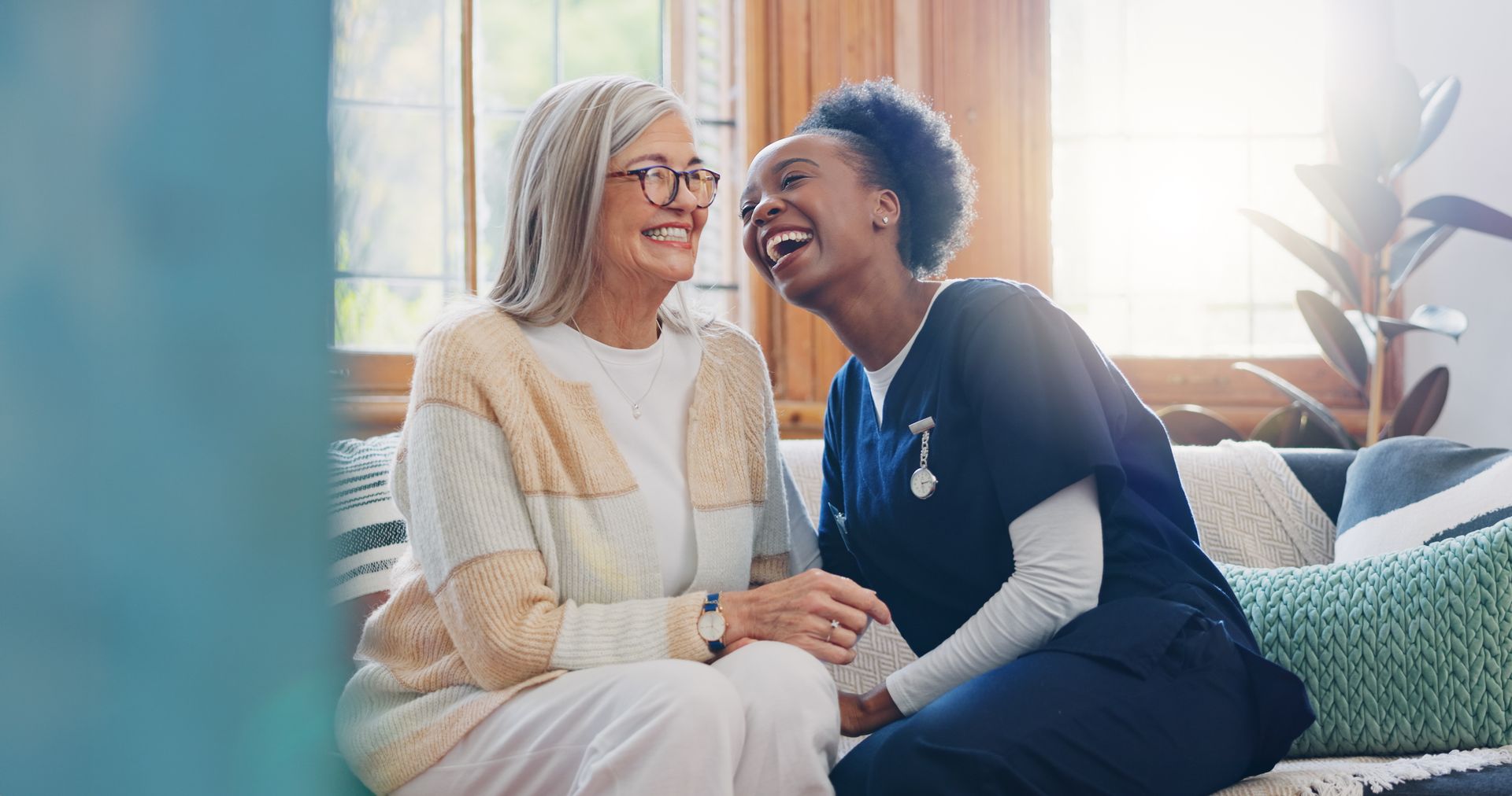 Woman in glasses laughs with healthcare worker indoors.