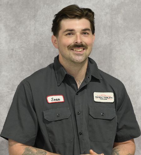 A man wearing a gray shirt with a name tag that says sean is smiling for the camera.