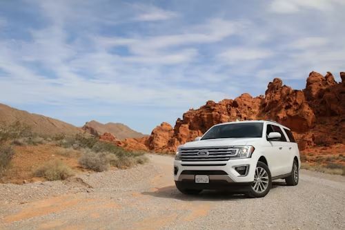 A white suv is parked on a dirt road in the desert.