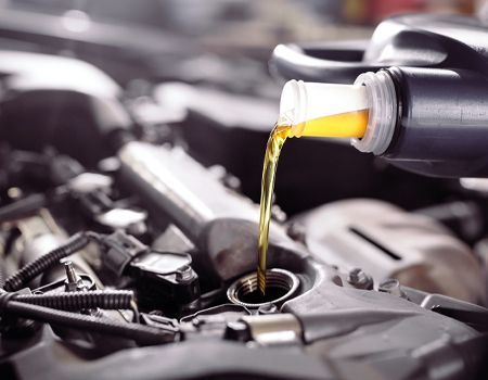 A close up of a person pouring oil into a car engine.