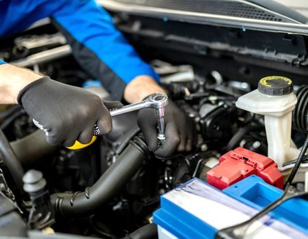 A man is working on the engine of a car with a wrench.