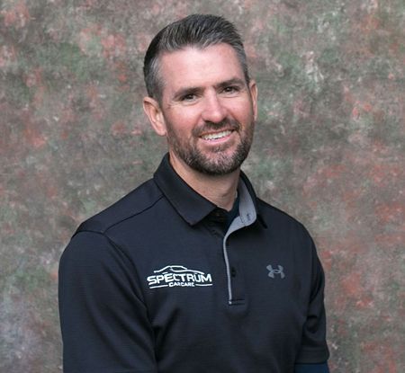 A man with a beard is wearing a black under armour polo shirt.