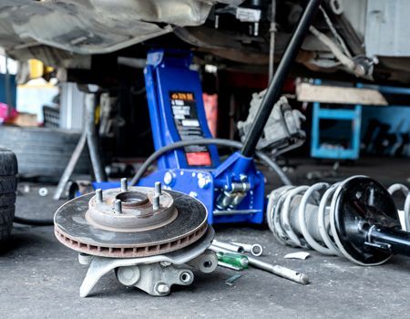 A car is being repaired in a garage with a blue jack.