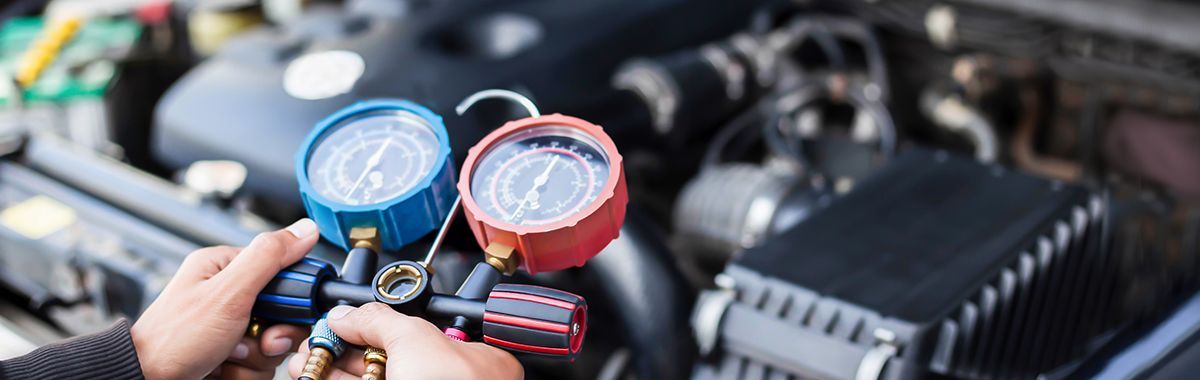 A person is holding two gauges in front of a car engine.