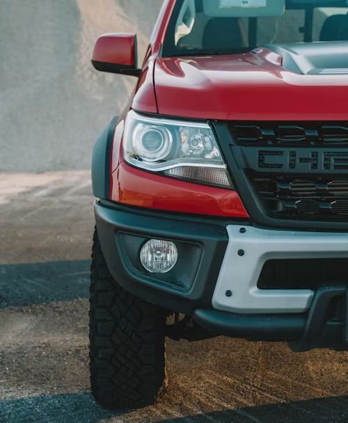 Red off-road truck front with headlight and tire on a dusty dirt road