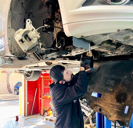 Mechanic working on a car from below, using a drill in a garage.