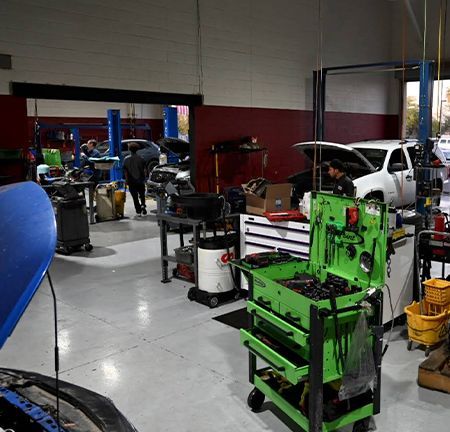 Auto repair shop interior with cars being worked on, tools, and mechanics.