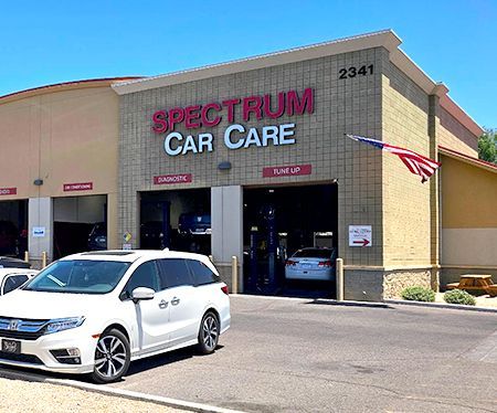 Spectrum Car Care auto shop exterior with parked white minivan. American flag.
