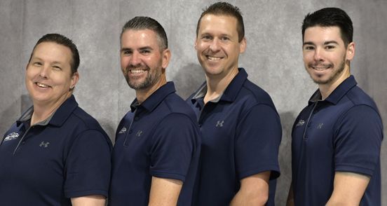 A group of four men wearing blue polo shirts are posing for a picture.